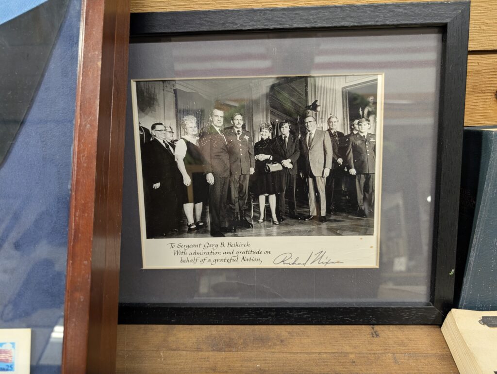 A framed black and white photograph showing President Richard Nixon presenting an award to Sergeant Gary B. Beikirch, surrounded by other individuals in military and civilian attire.