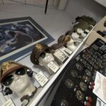 A museum exhibit of World War II U.S. Army Air Forces flight gear, including officer hats, aviator sunglasses, and flight helmets displayed on mannequin heads next to an aircraft instrument panel.