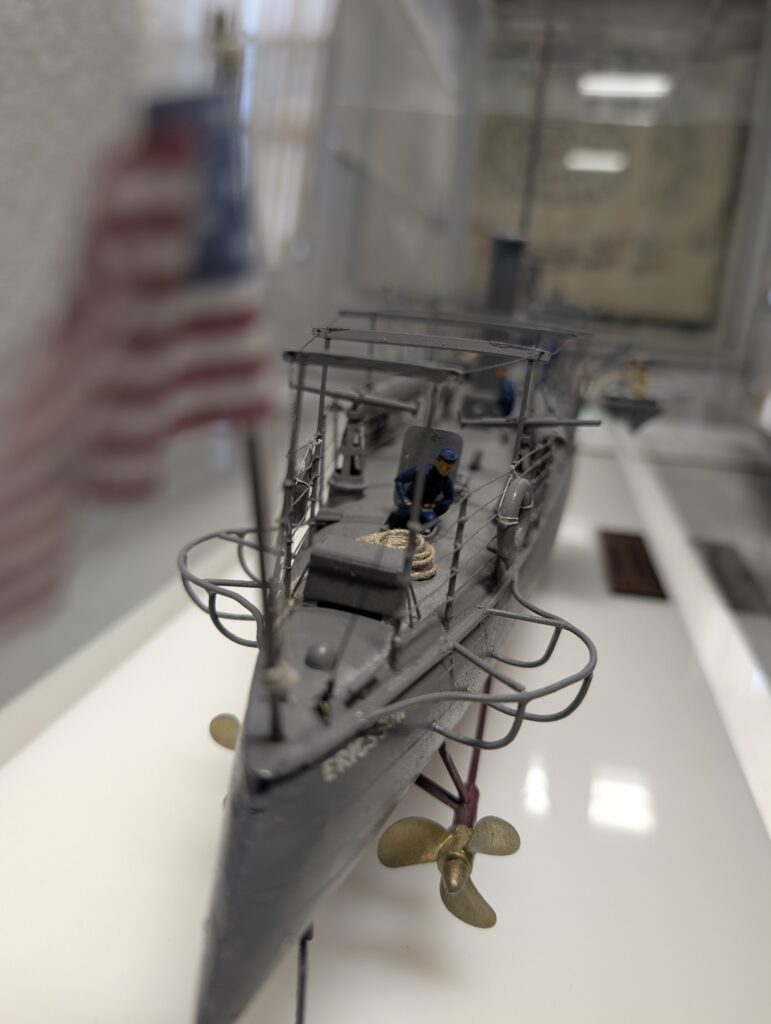 A detailed scale model of the USS Ericsson, a late 19th-century U.S. Navy torpedo boat, viewed from the bow inside a display case.
