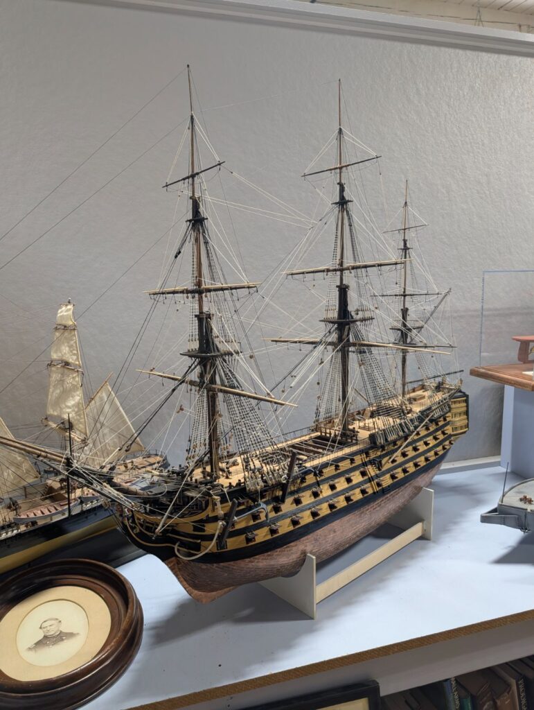 A highly detailed wooden model of a three-masted sailing warship with multiple gun decks, displayed alongside other maritime artifacts.