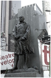 A bronze statue of a soldier in front of a large cross-shaped monument.